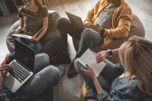 Four millennials sitting around on bean bags with laptops and notepads